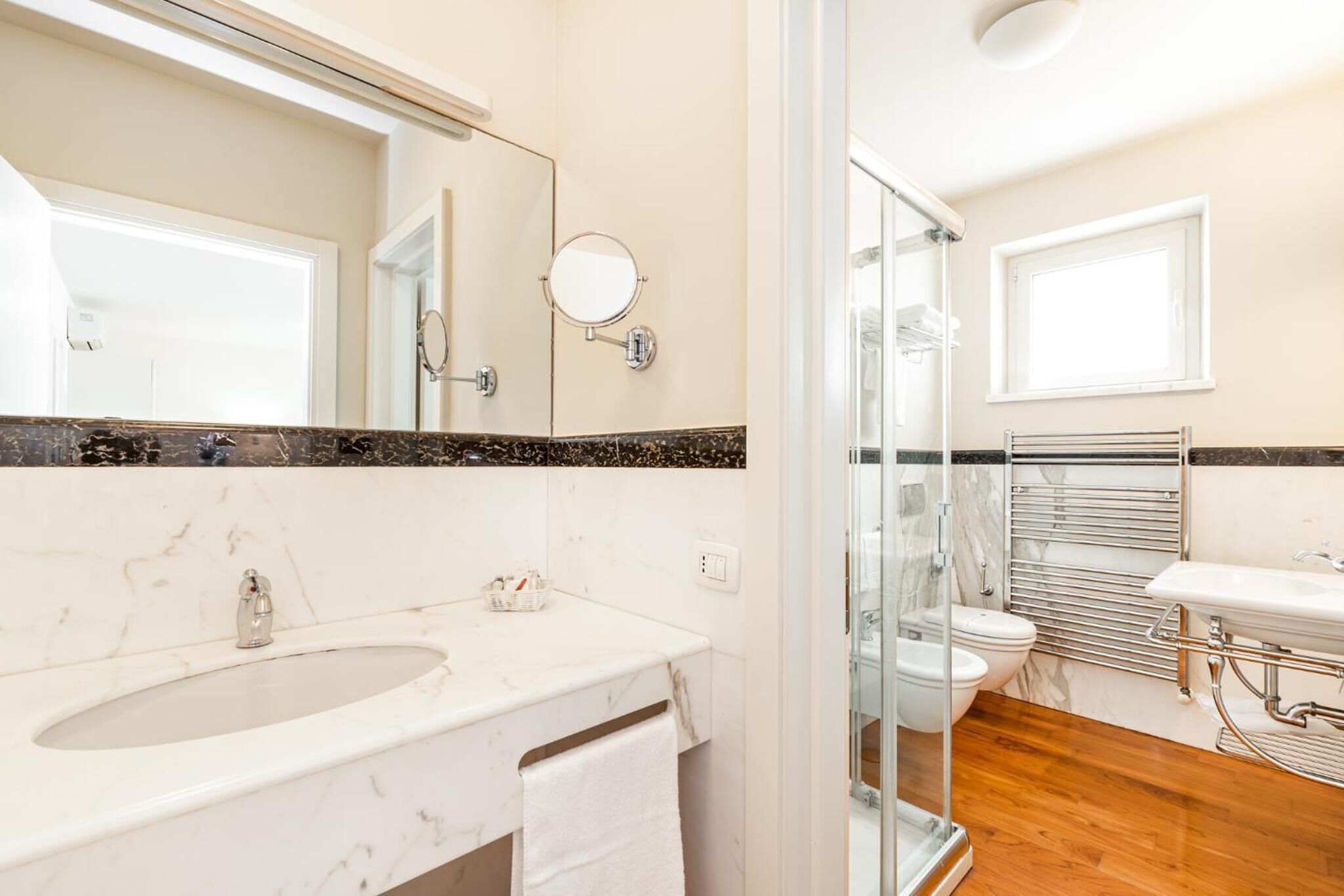 A bathroom with a marble sink, a large mirror, a glass shower enclosure, and a white toilet.