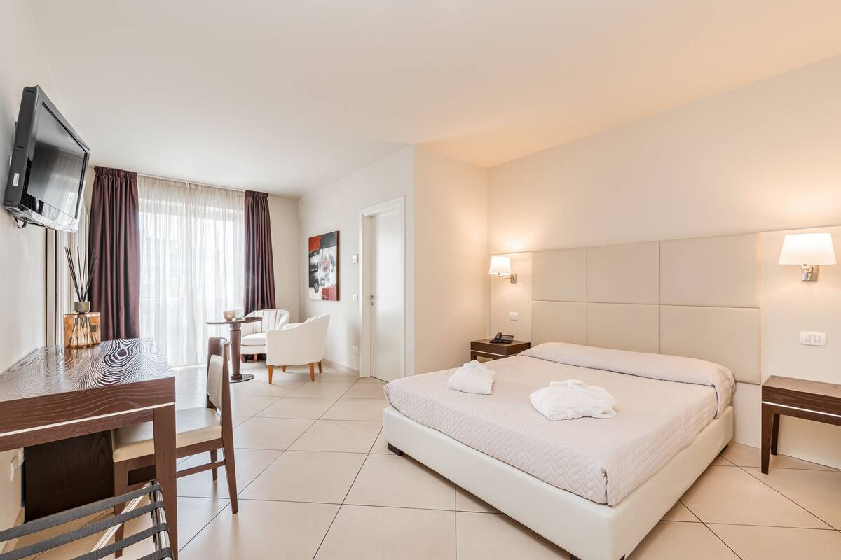 A hotel room with a bed, a desk with a chair, a TV, and a small table with a lamp.