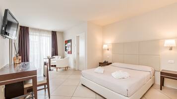 Una camera d'albergo con un letto, una scrivania con una sedia, una televisione e un tavolino con una lampada.