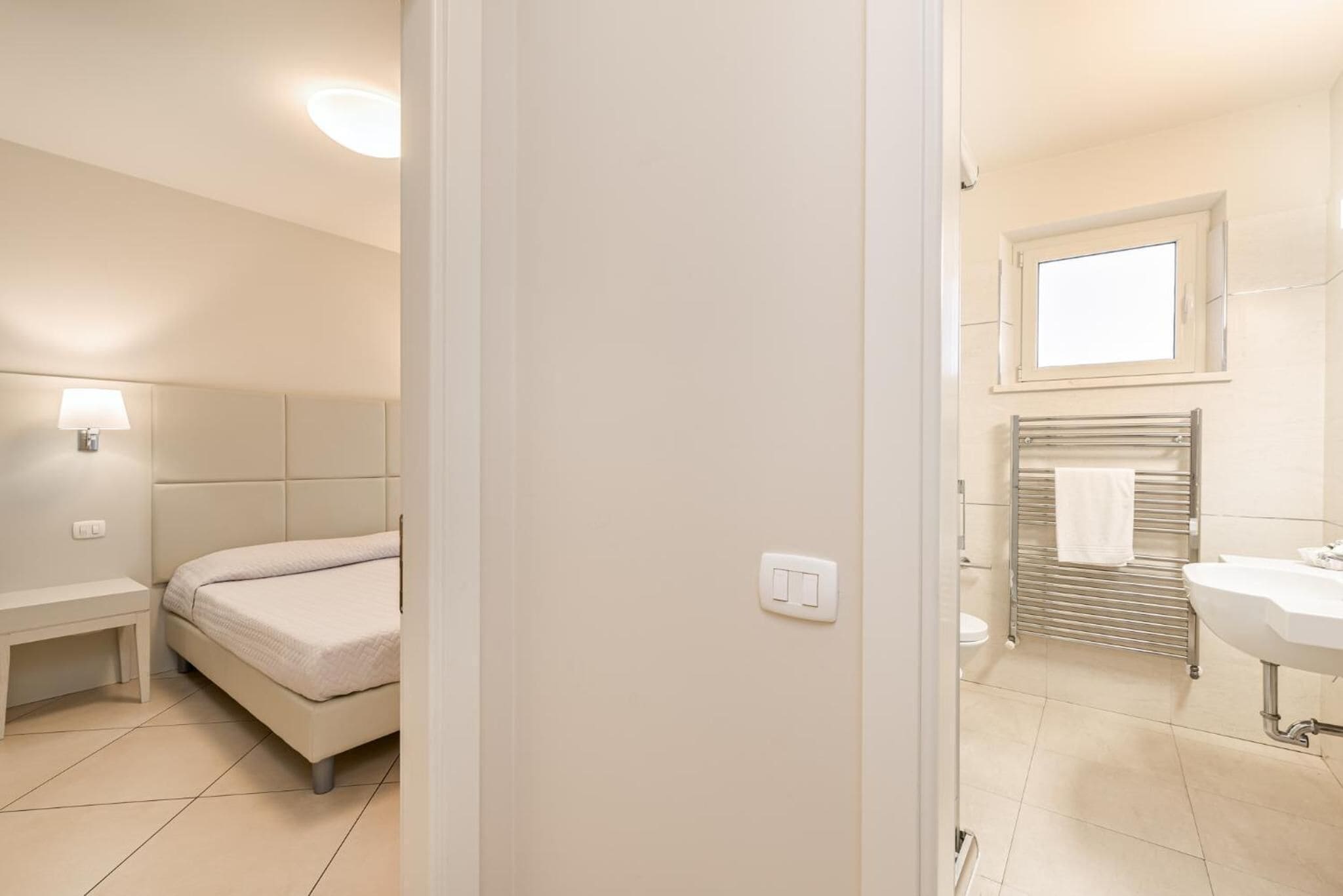 A bedroom with a bed, bedside table, and a nightstand. The room has a light switch and a power outlet on the wall.