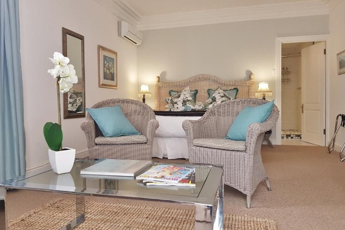 A living room with two wicker sofas, a glass coffee table, a white potted plant, and a framed picture on the wall.