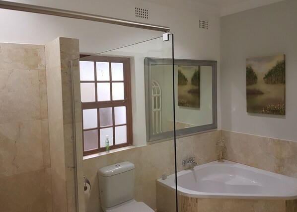 A bathroom with a bathtub, toilet, and a window with frosted glass.