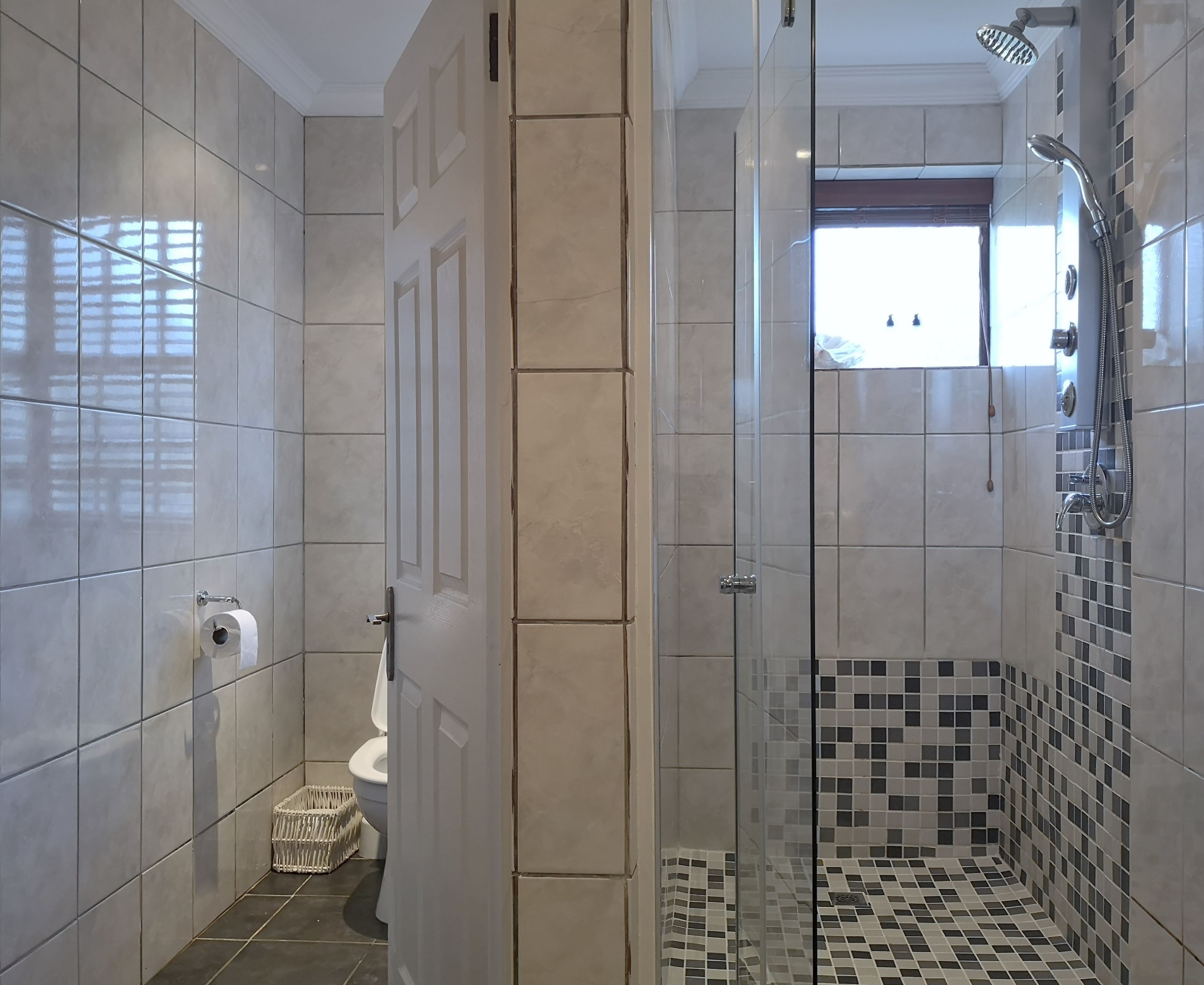 A modern bathroom with a glass-enclosed shower, a toilet, and a small wicker basket.