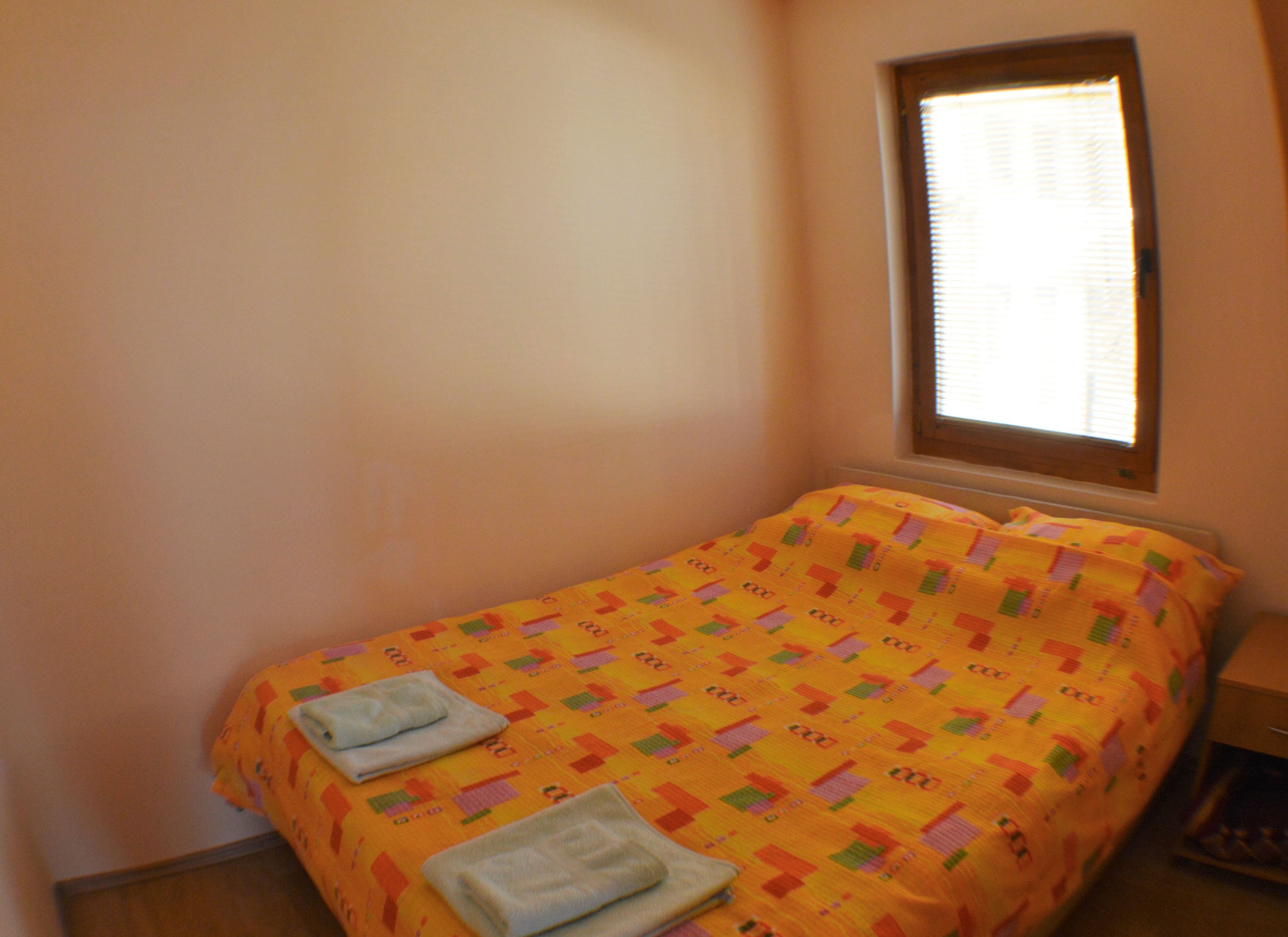 Quarto pequeno com uma cama de solteiro, um edredom colorido e duas toalhas dobradas cuidadosamente.