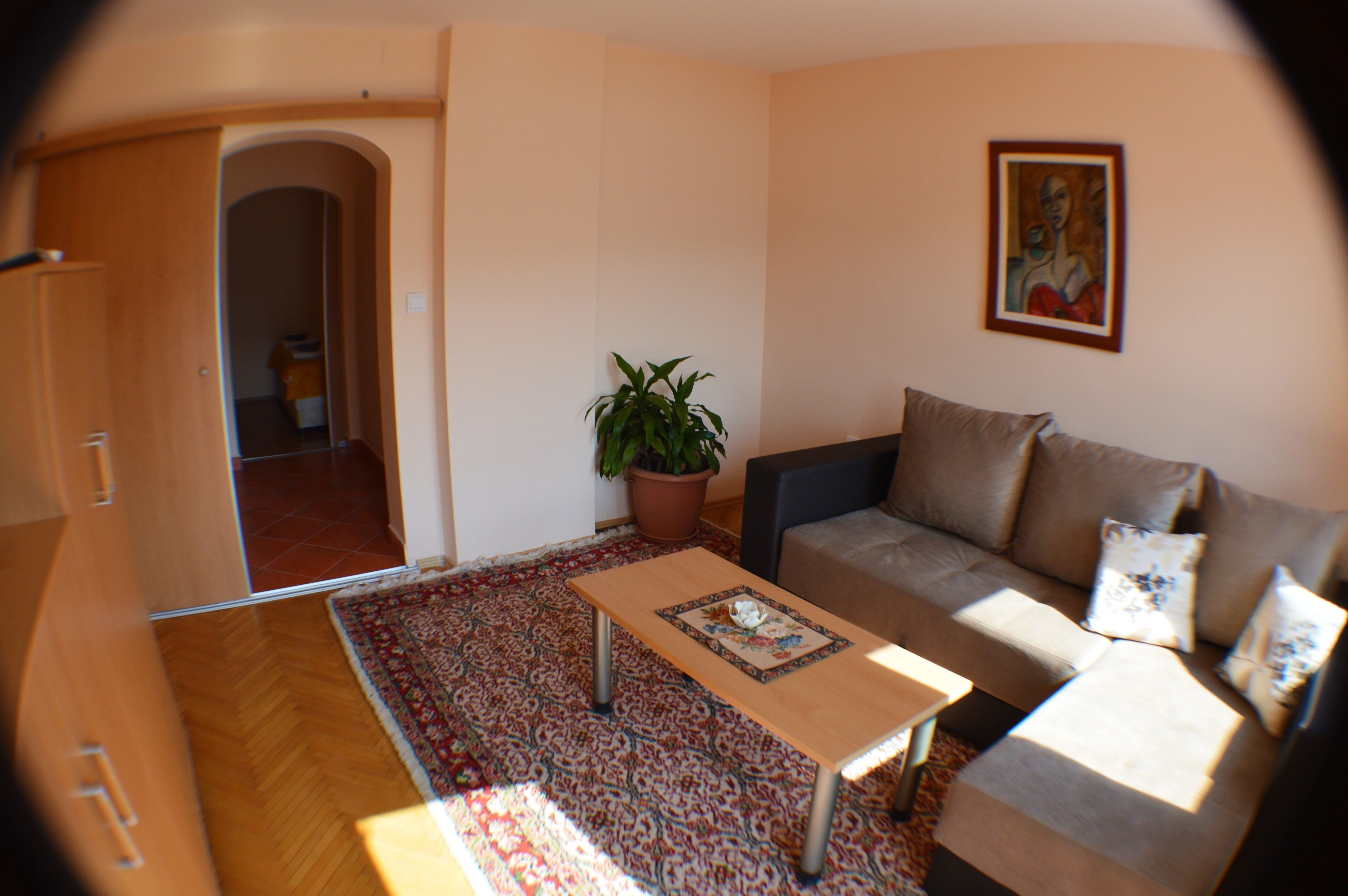 A living room with a sofa, a coffee table, a potted plant, and a painting on the wall.