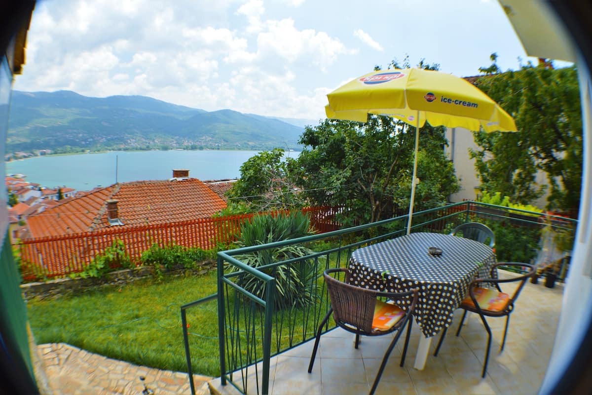 A patio with a table and chairs, a yellow umbrella, and a view of a lake and mountains.