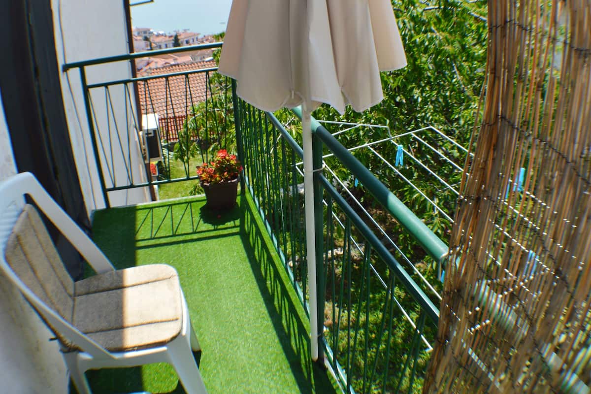 A balcony with a white chair, a beige umbrella, and a potted plant.