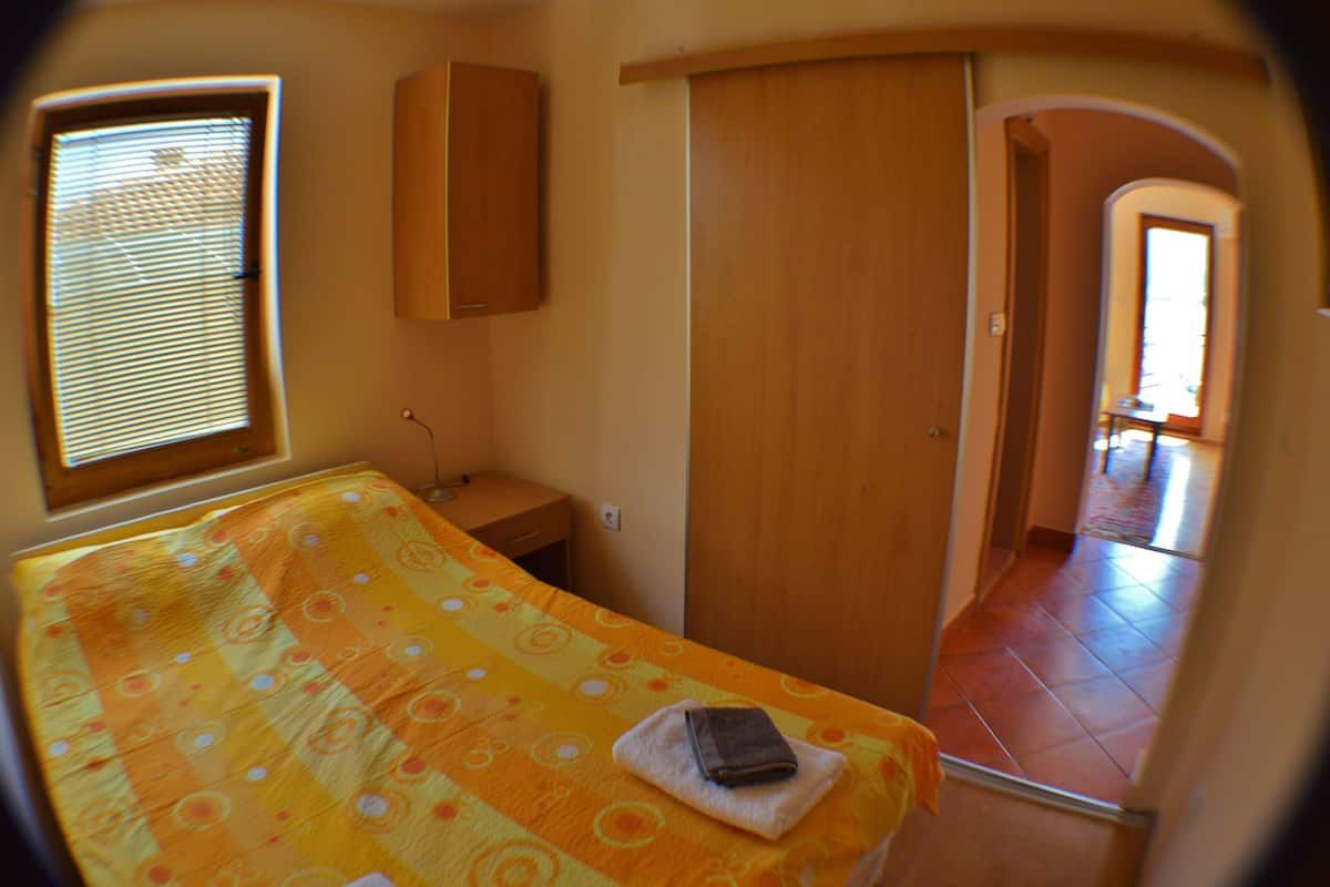 A room with a bed, a wardrobe, a small table, and a window.