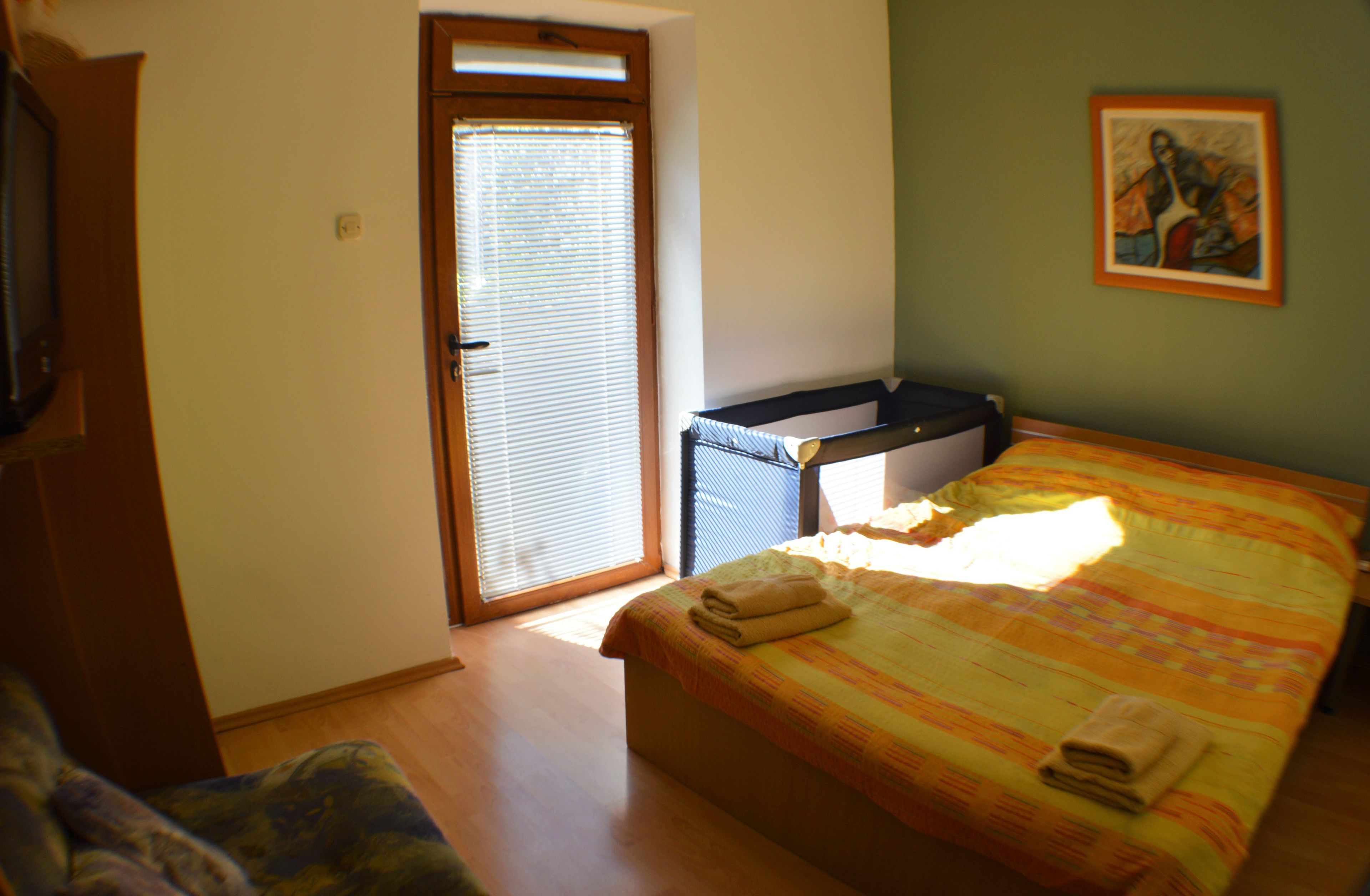 A bedroom with a bed, a chair, a window with blinds, and a door.