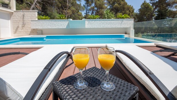 A poolside area with two lounge chairs and two glasses of orange juice on a woven table. - Villa Fani - Apartments and Rooms (Trogir)