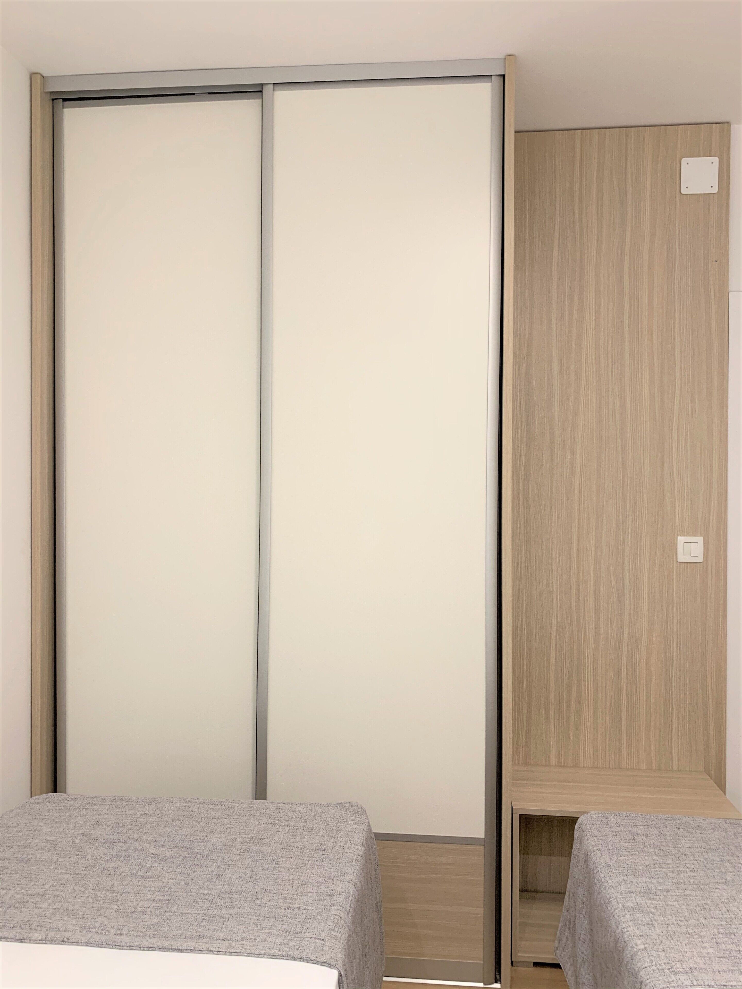 A bedroom with two beds, a sliding door, and a wooden wardrobe.