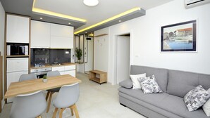A modern living space with a dining area, kitchen, and a grey sofa with floral cushions. - Villa Fani - Apartments and Rooms (Trogir)