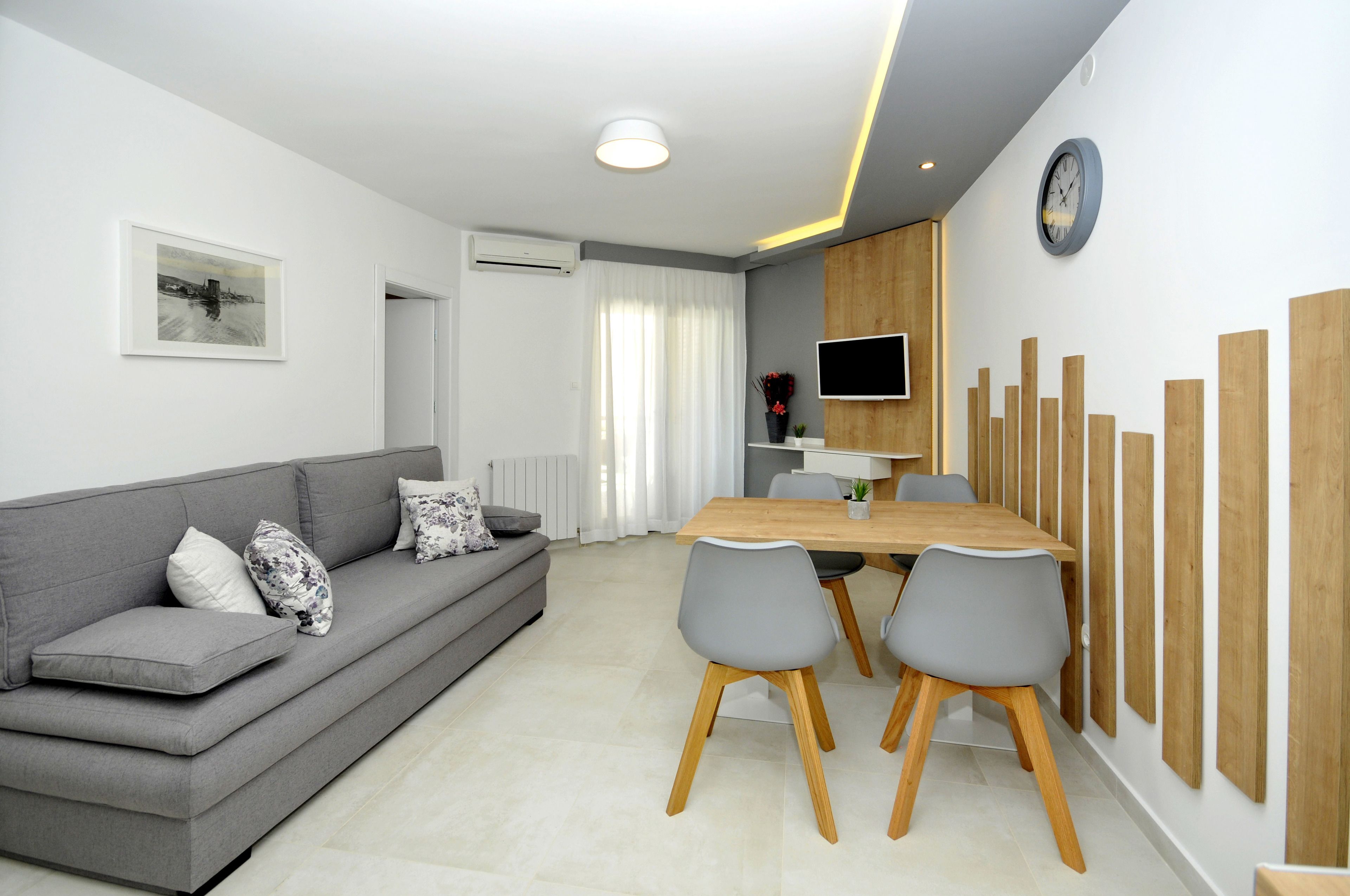 A modern living room with a grey sofa, a wooden dining table, and grey chairs.