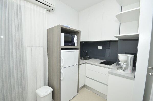 Una cocina compacta con microondas, cafetera y lavabo.