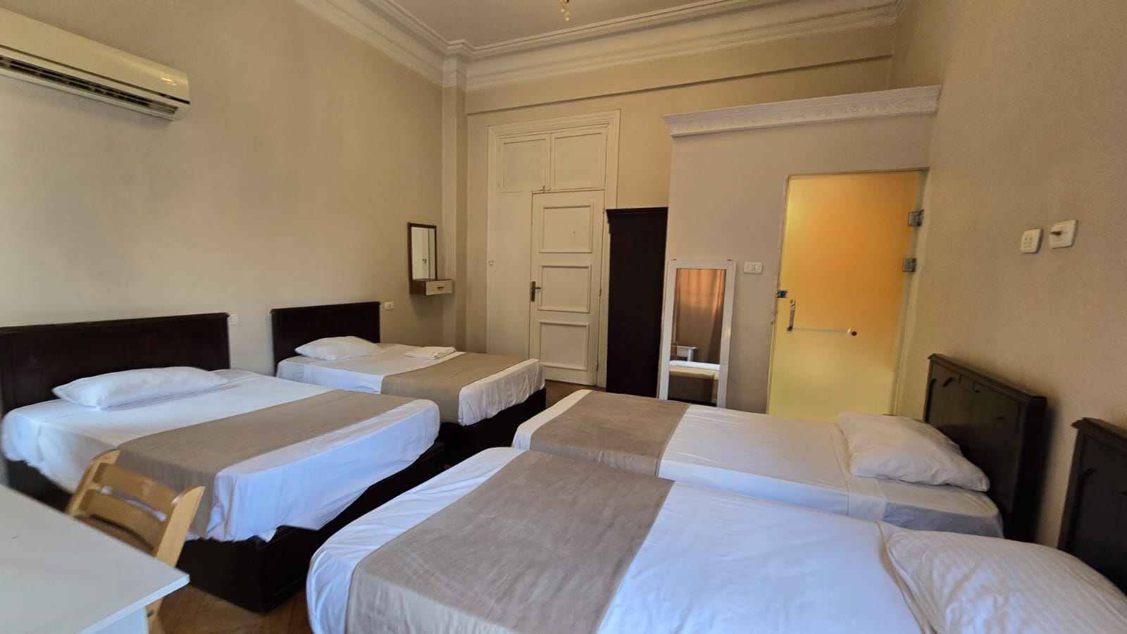 A hotel room with four single beds, a desk, and a chair.