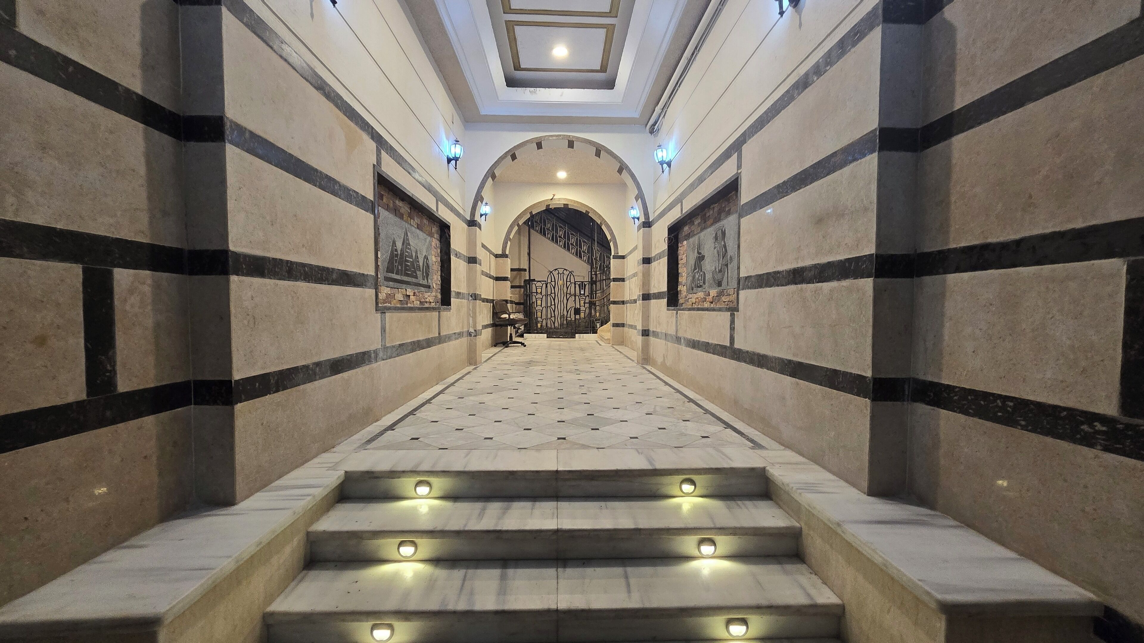 A grand hallway with a marble floor, leading to a staircase with illuminated steps.