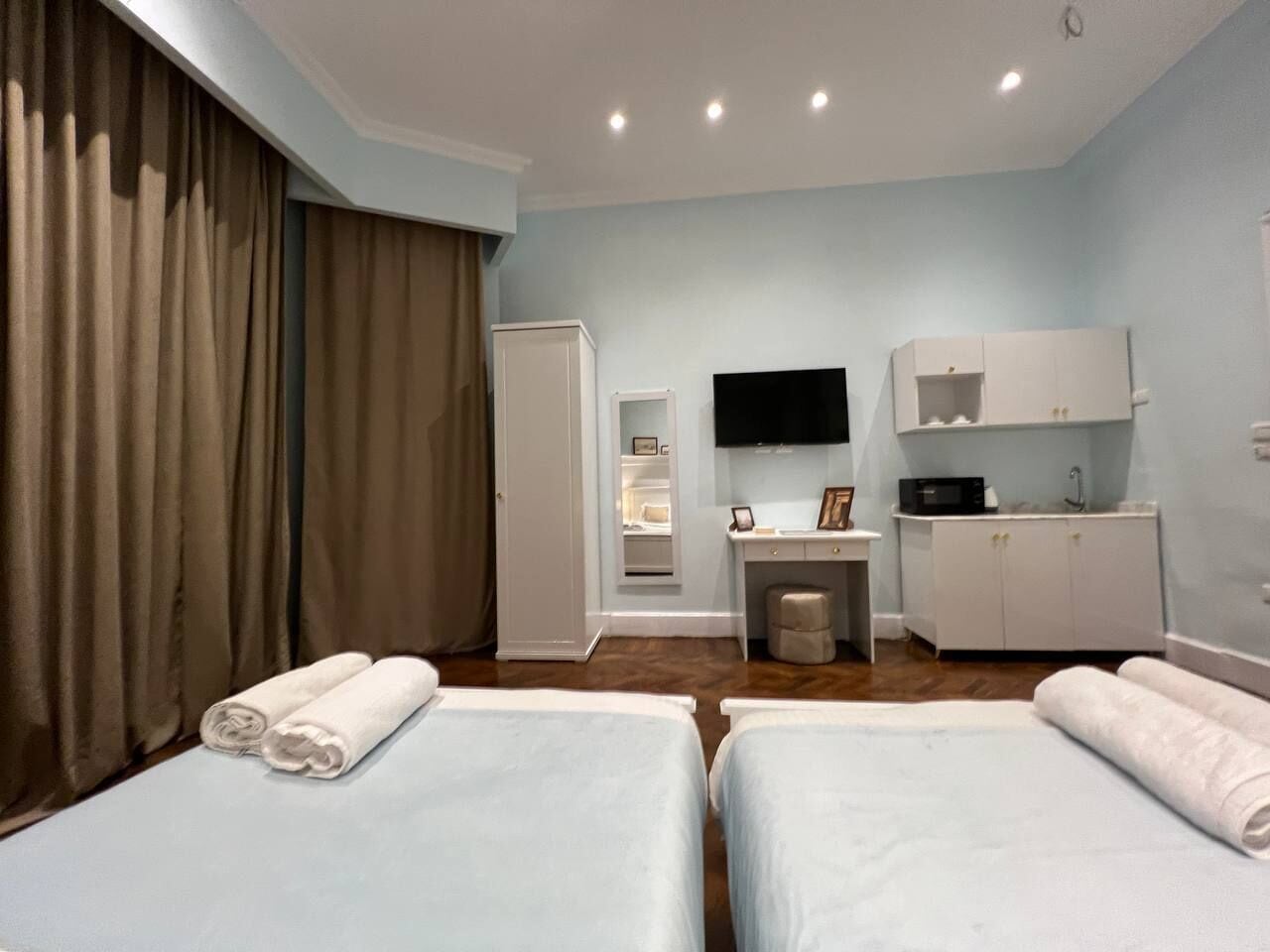 A hotel room with two beds, a TV, a desk, and a kitchenette.