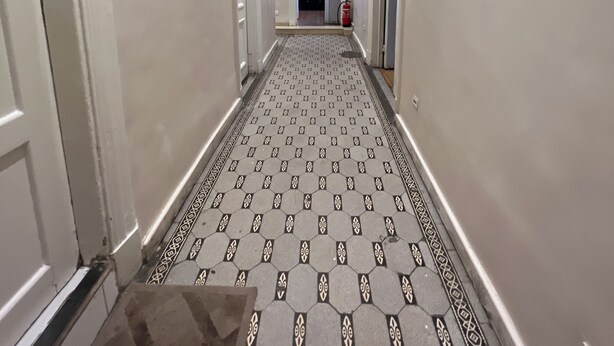 Un pasillo con suelo estampado, paredes blancas y puertas que dan a habitaciones.