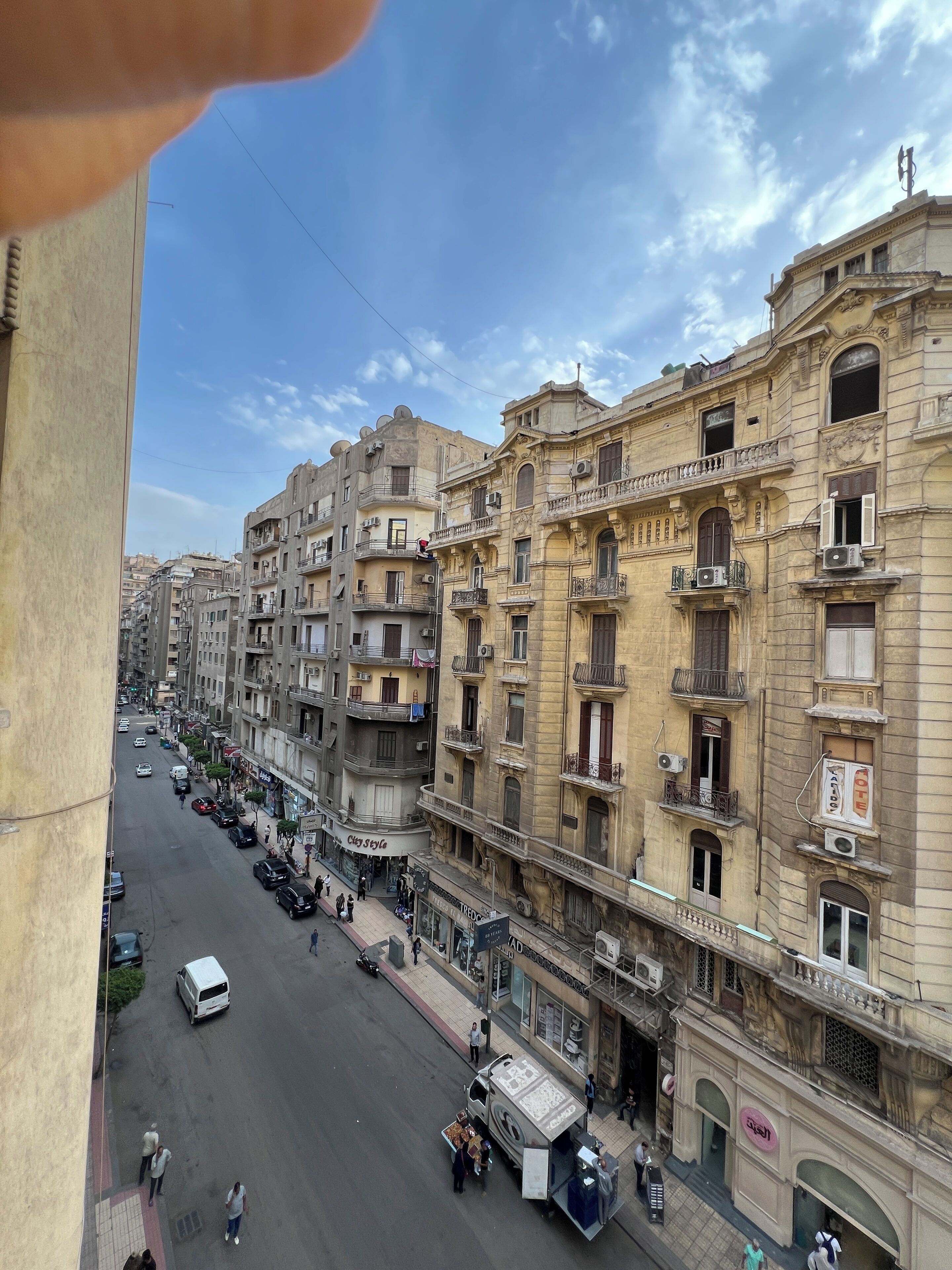 Vista da rua com edifícios altos, uma van branca e pedestres.