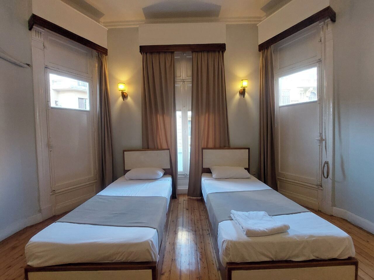 Ein Zimmer mit zwei Einzelbetten, Holzboden und zwei mit Vorhängen versehenen Fenstern.