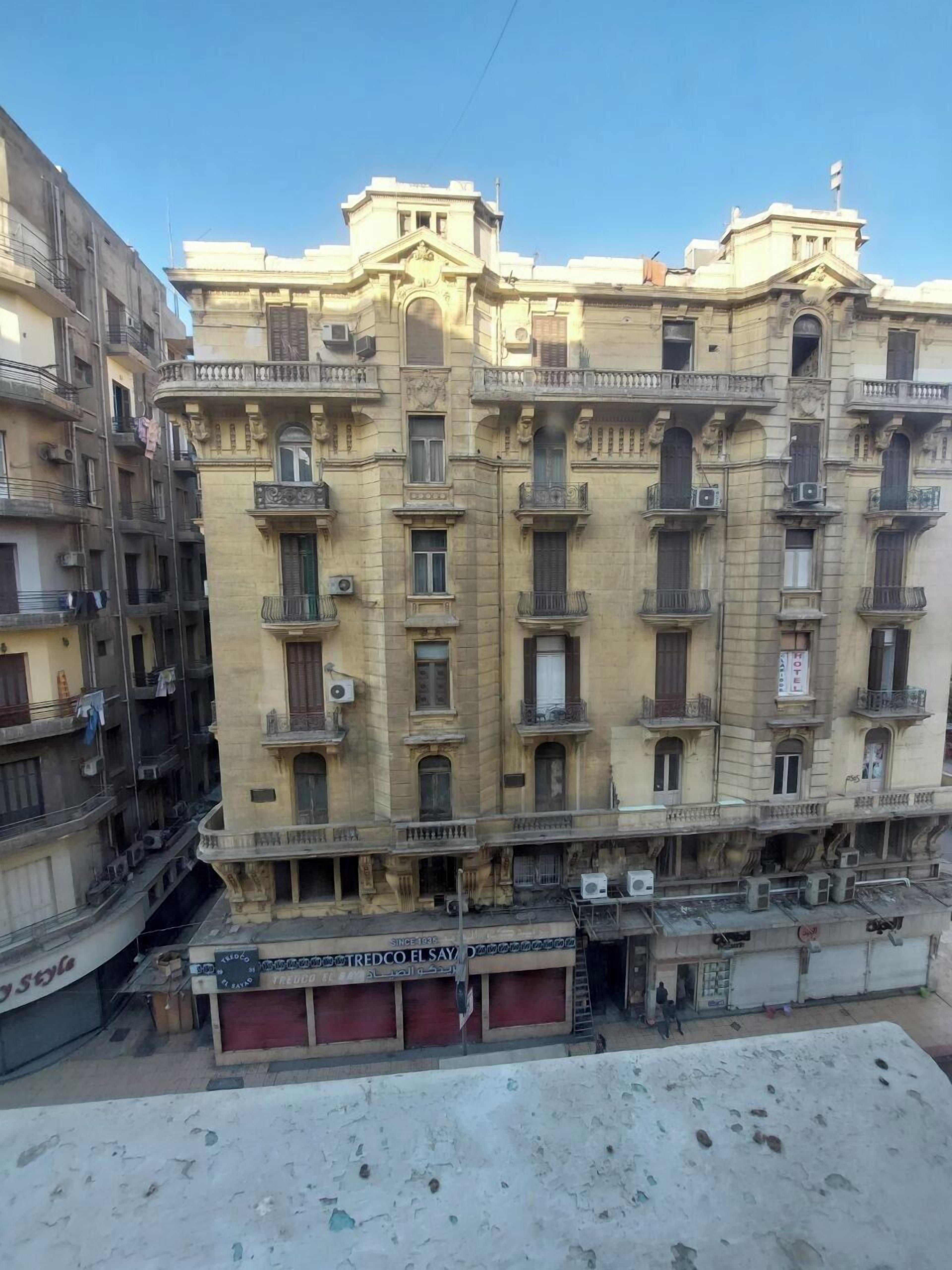 Un edificio de varios pisos con balcones, equipos de aire acondicionado y una tienda en la planta baja.