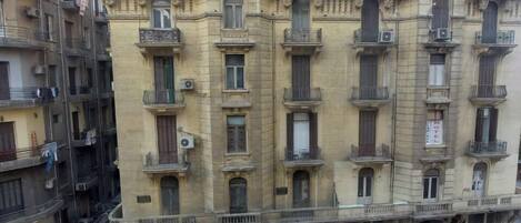 Un edificio de varios pisos con balcones, equipos de aire acondicionado y una tienda en la planta baja.