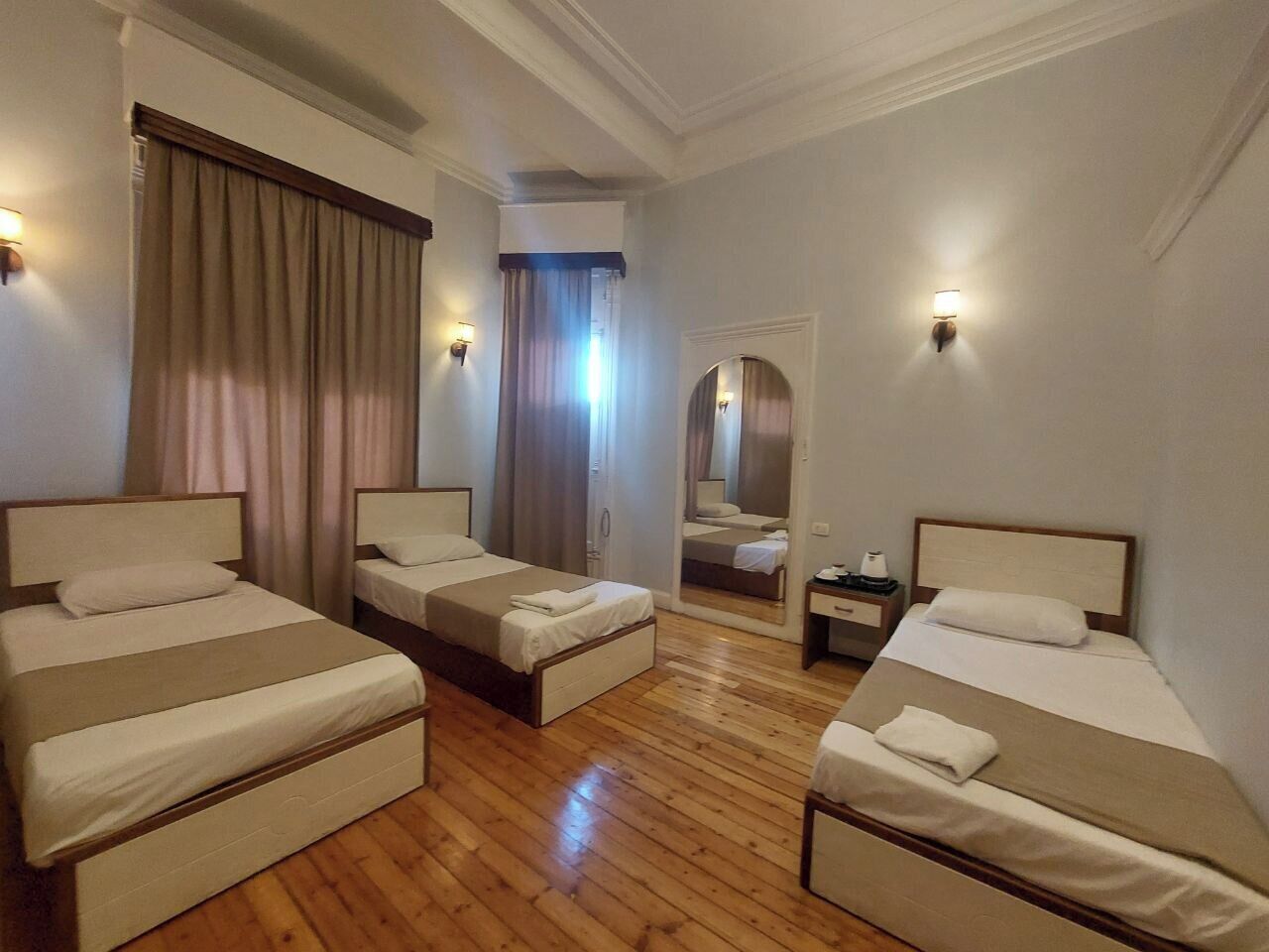 Una habitación de hotel con tres camas individuales, suelo de madera y un espejo en la pared.