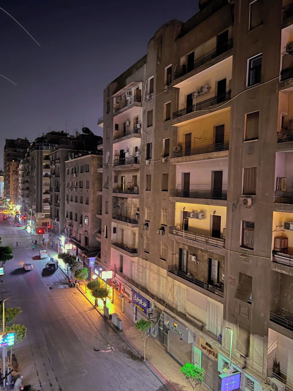 Un edificio de varios pisos con balcones, una calle delante y letreros iluminados.