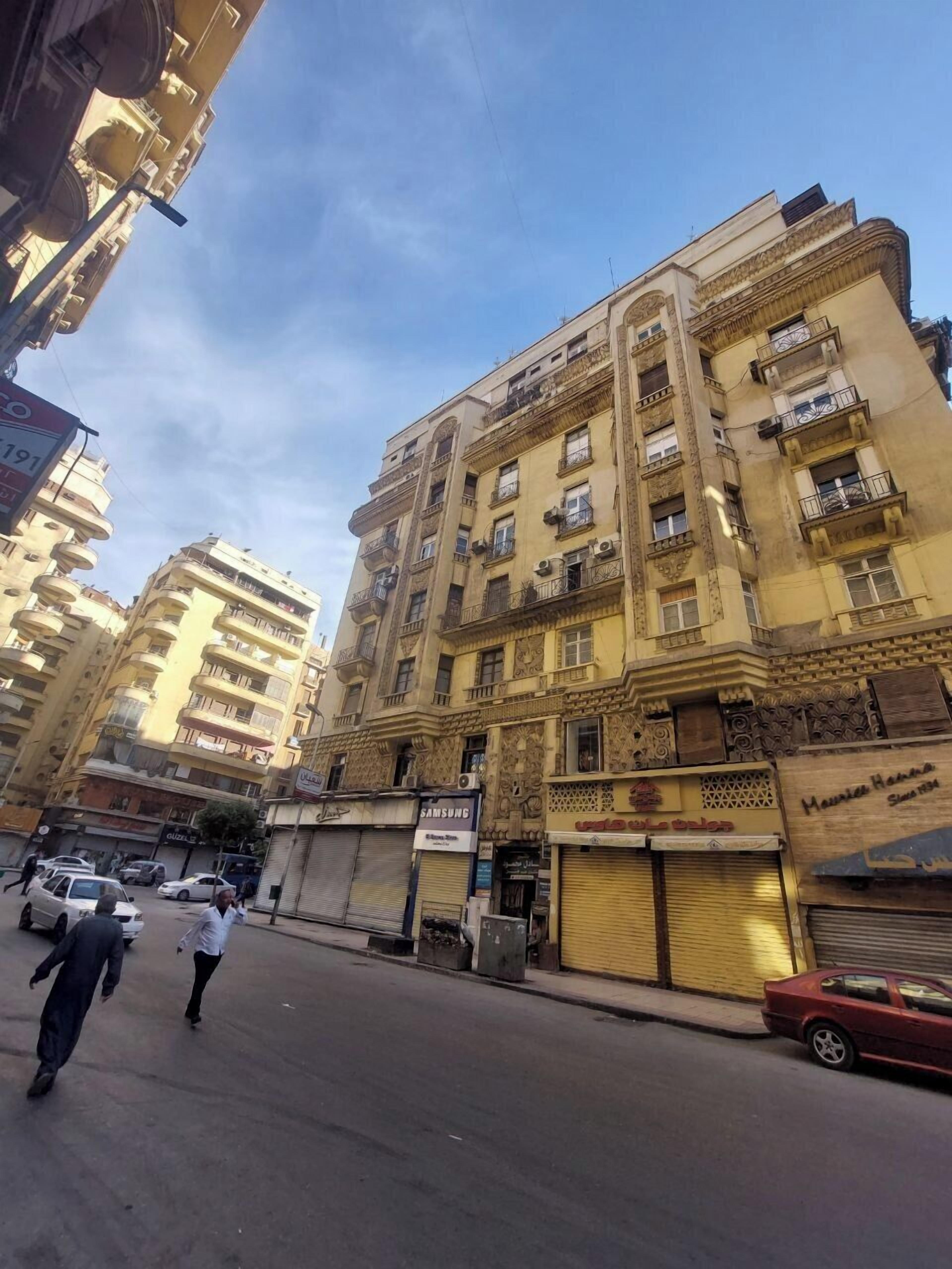 Un edificio de varios pisos con balcones, una tienda Samsung y un comercio con la persiana baja.