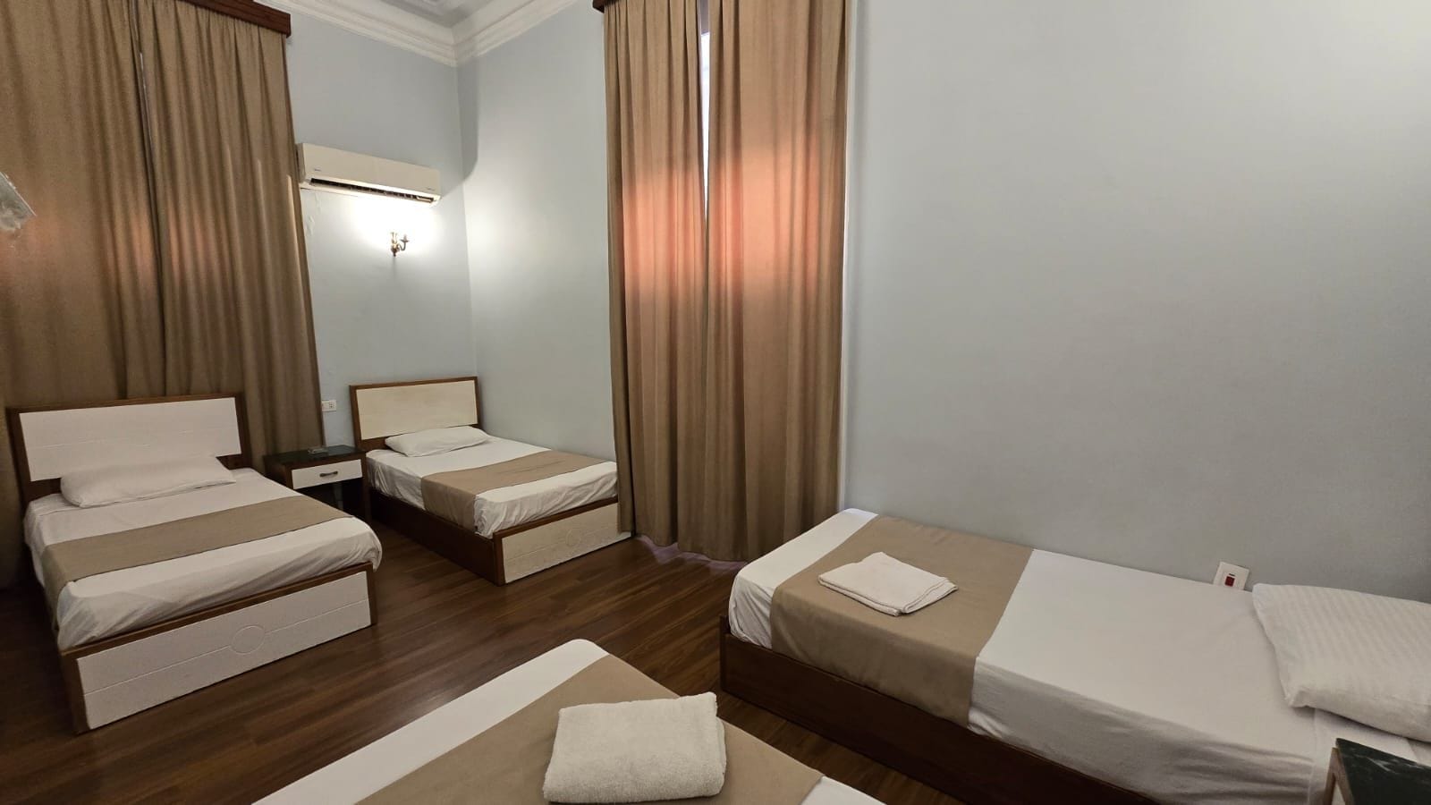 Ein Hotelzimmer mit zwei Betten, einem Nachttisch, einer Lampe und einem Fenster mit Vorhängen.