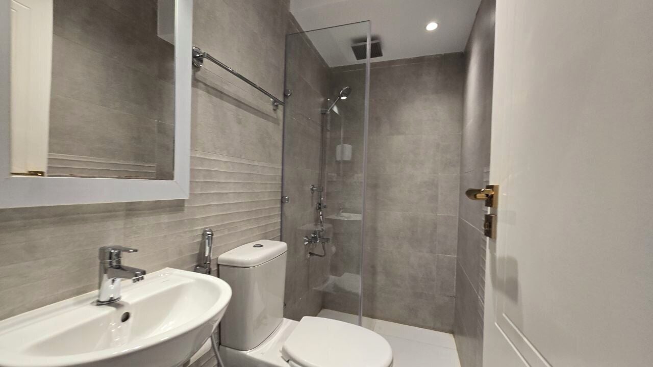 Un baño moderno con cabina de ducha de vidrio, un lavabo blanco y un inodoro.