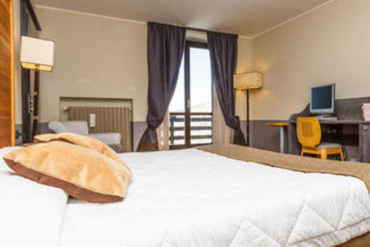 A hotel room with a bed, a desk, a chair, a lamp, and a picture on the wall.