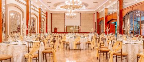 A banquet hall with round tables, chairs, and a chandelier.