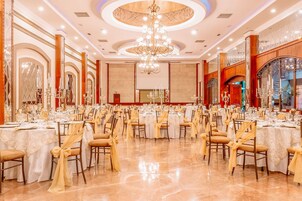 A banquet hall with round tables, chairs, and a chandelier.