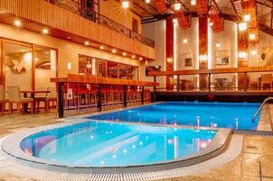 Vestíbulo de hotel con una amplia piscina interior, zona de bar y área de descanso con mesas y sillas.