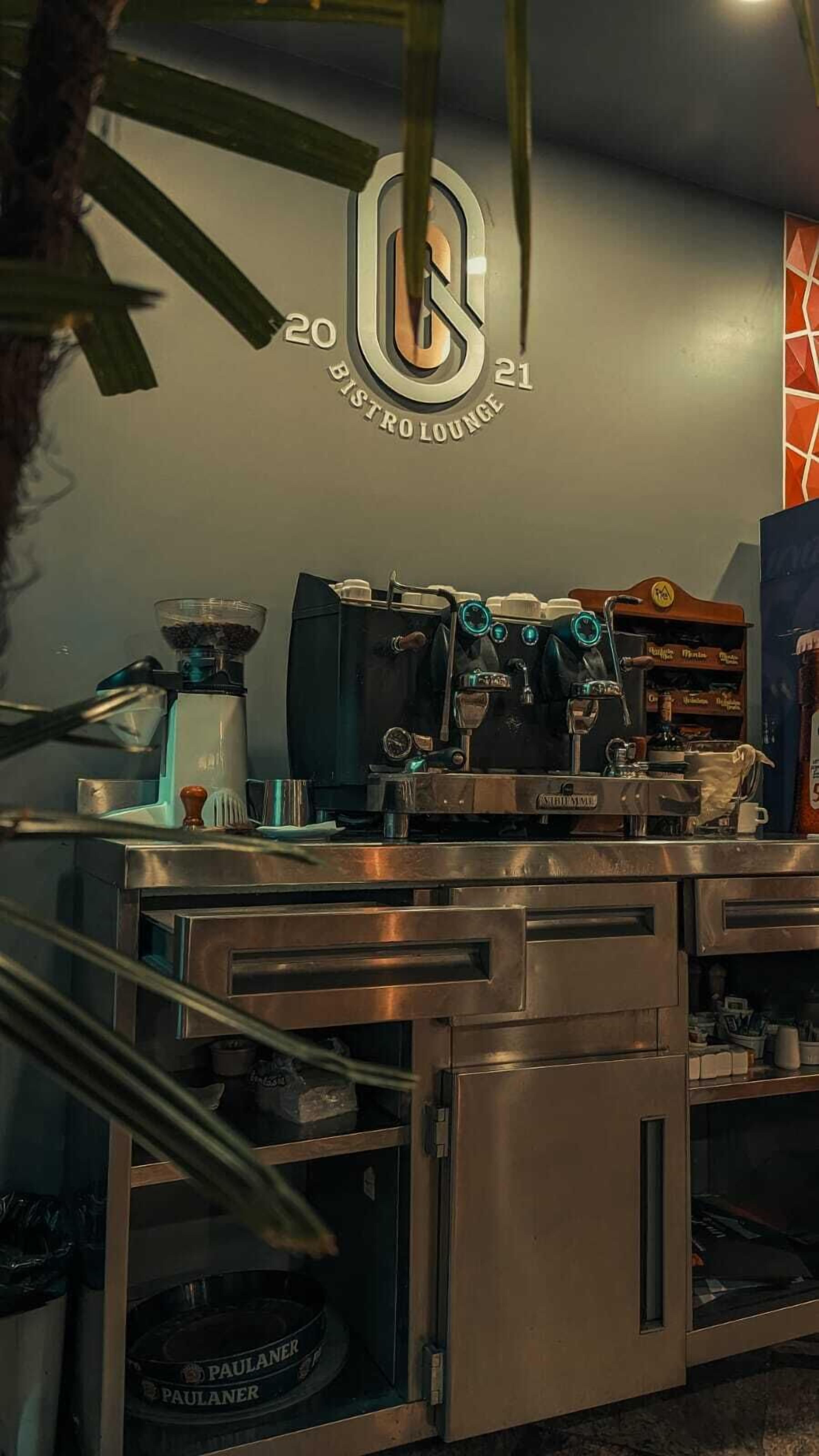 A coffee bar with espresso machines and a coffee grinder, a sign for Bistro Lounge, and a refrigerator with a beer tap.