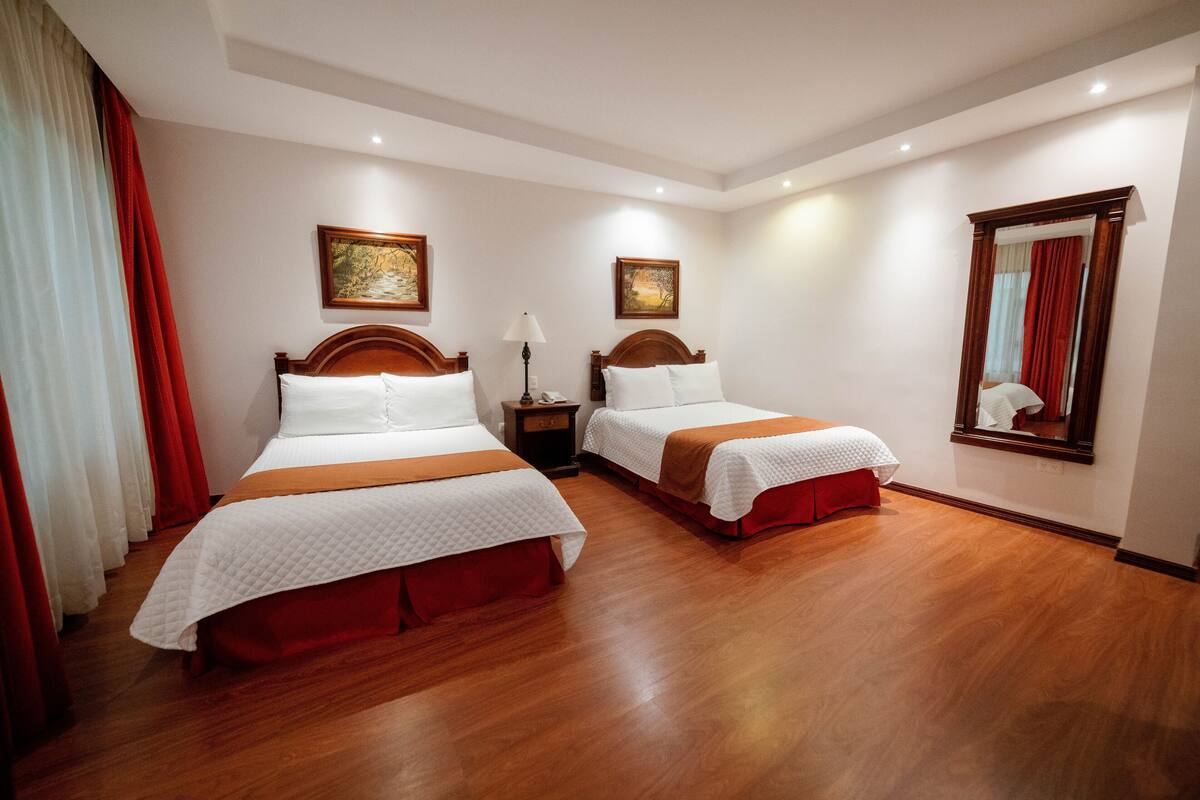 Ein Hotelzimmer mit zwei Betten, Holzboden und einem großen Spiegel an der Wand.