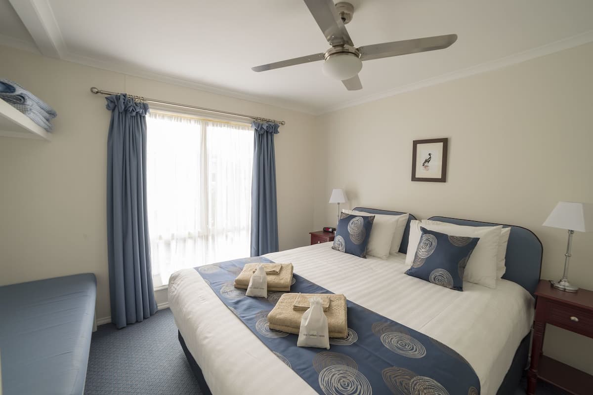 A hotel room with a large bed, a ceiling fan, a bedside table with a lamp, a framed picture on the wall, and a window with curtains.