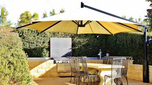 An outdoor kitchen with a grill, dining table, and chairs under a large umbrella. - Tokemata Retreat (Cobram East)