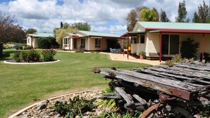 A row of single-story houses with green roofs, a paved driveway, and a garden area with a wooden cart. - Tokemata Retreat (Cobram East)