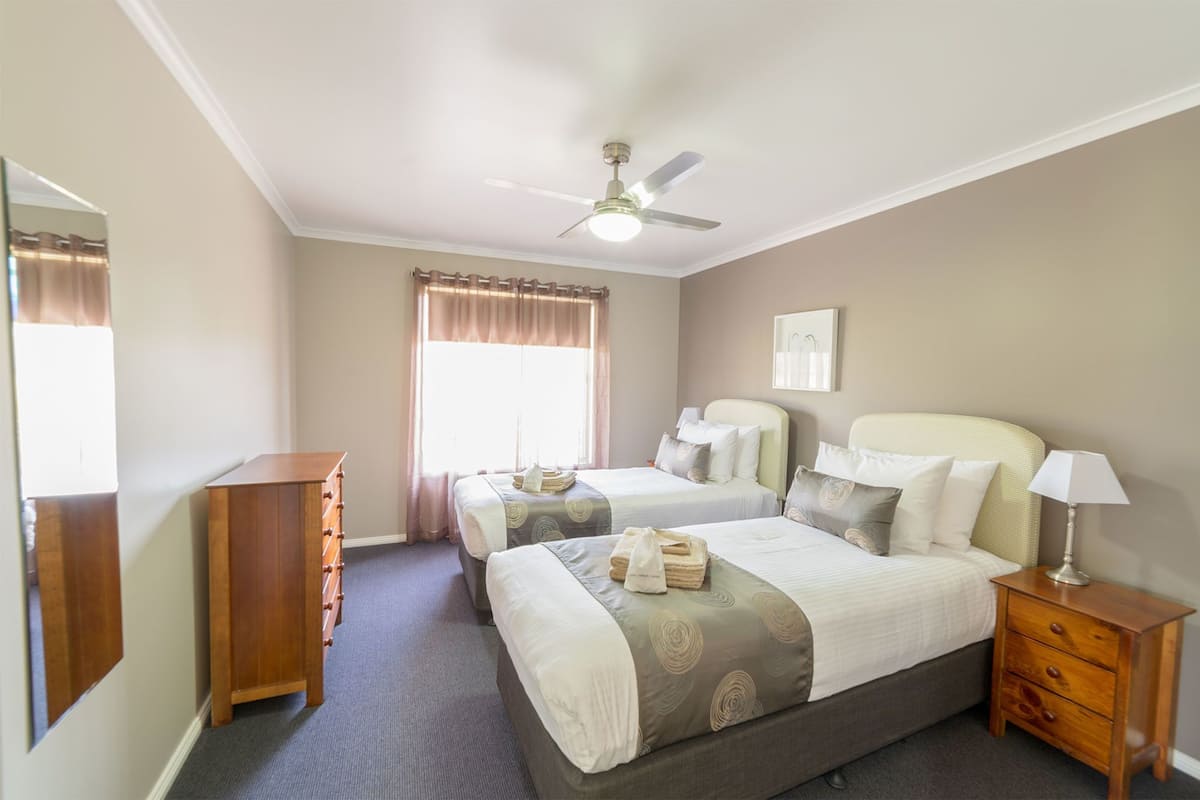 A hotel room with two beds, a ceiling fan, a dresser, a nightstand, and a window with curtains.