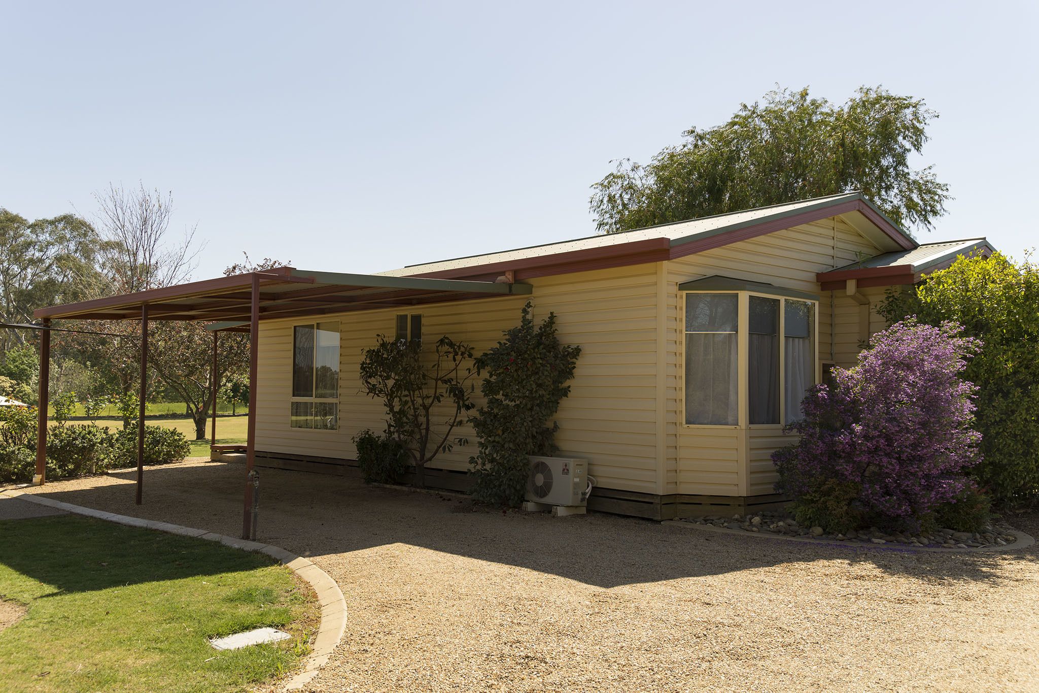Ein Bungalow mit überdachter Veranda, einem kleinen Garten und einem Schotterweg.