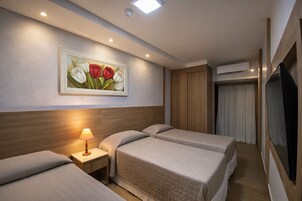 Et hotelværelse med to senge, et natbord med lampe, et blomsterbillede, en aircondition og et fjernsyn.