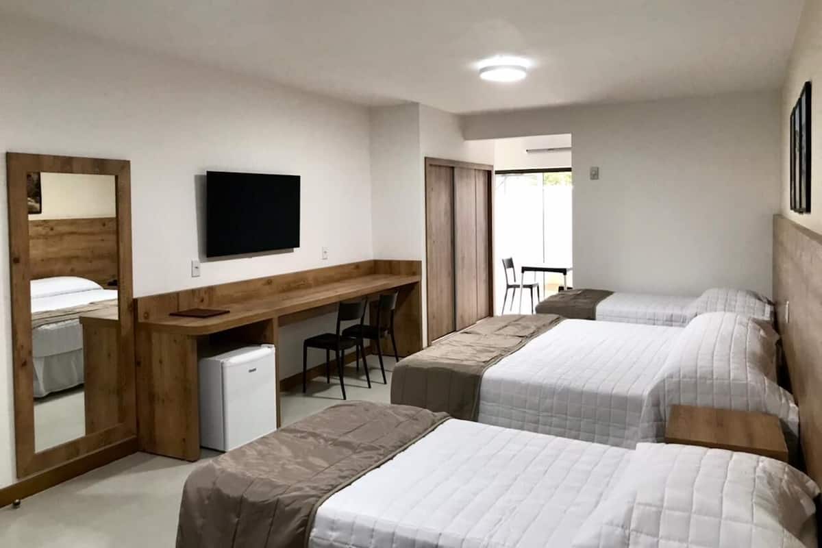 A hotel room with three beds, a desk with a chair, a television, and a small refrigerator.