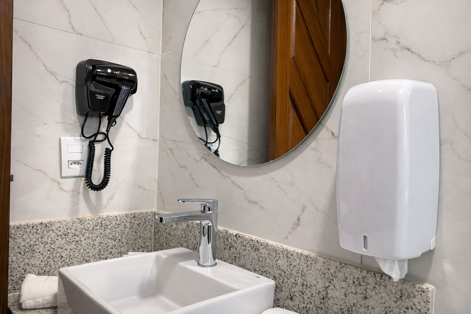 A bathroom with a white sink, a mirror, a hair dryer, and a hand dryer.