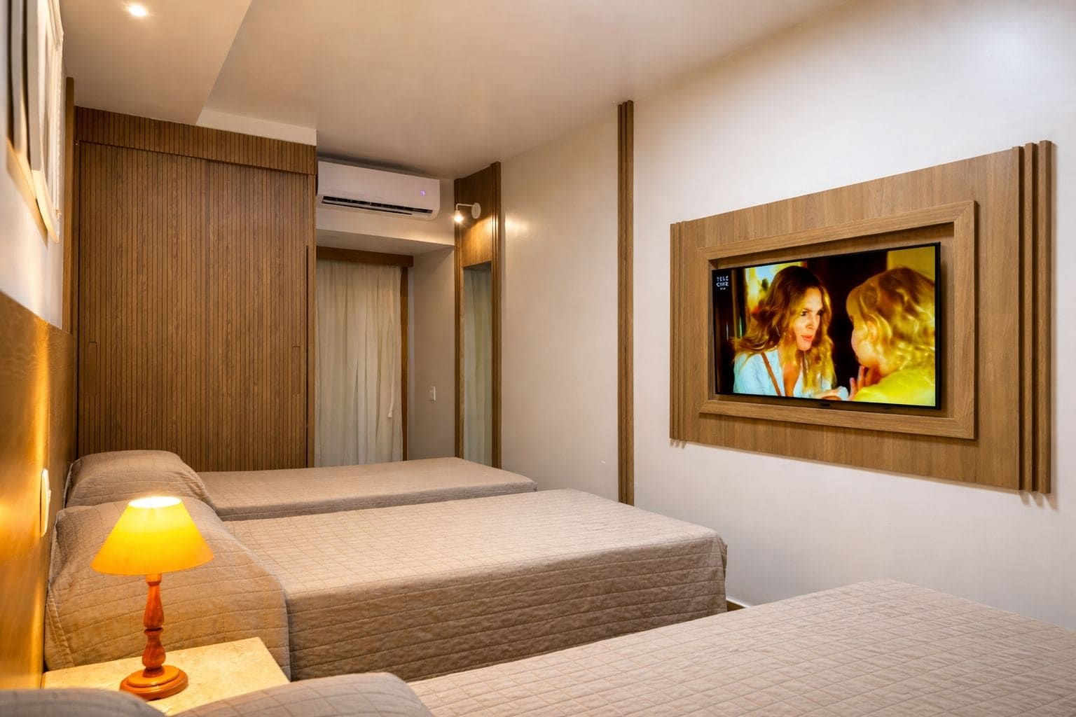 A hotel room with two beds, a wall-mounted TV, and an air conditioning unit.
