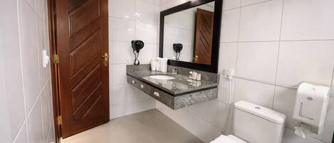 Un baño moderno con puerta de madera, encimera de mármol, espejo grande, inodoro y secador de manos.