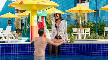 A pool area with a tiled blue floor, yellow umbrellas, and a colorful play structure.