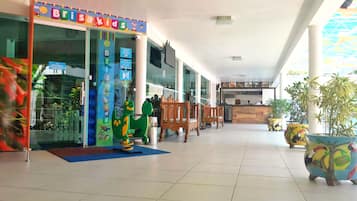 A children's play area with a dinosaur ride, wooden chairs, and a reception desk.
