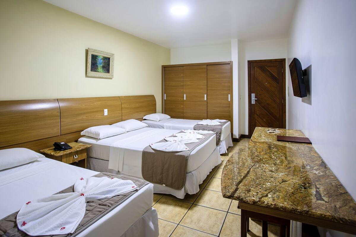 A hotel room with two beds, a wooden headboard, a painting on the wall, a wardrobe, and a granite countertop.